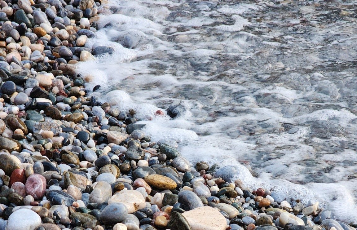 an image with smooth rocks with water lapping at the edge