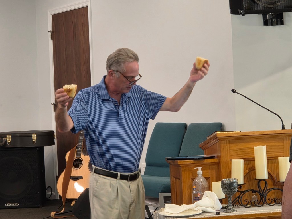 Pastor holding broken bread during Communion at Rock & Refuge Church